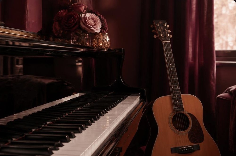 Grand piano and acoustic guitar in a room with deep red curtains